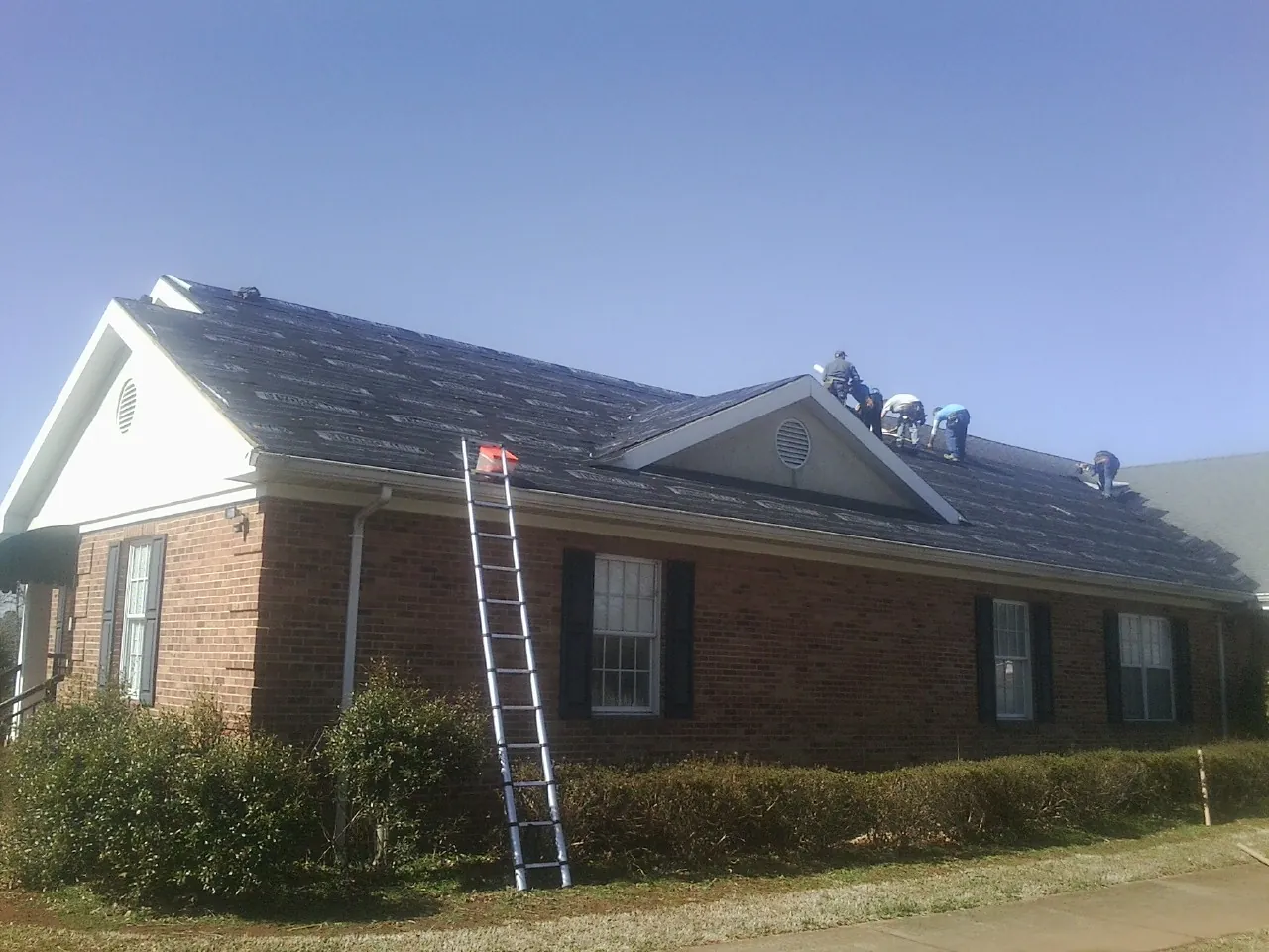 Crew tearing shingles off a brick ranch roof with a ladder set — Emergency Roof Repair work by our crew in Albion